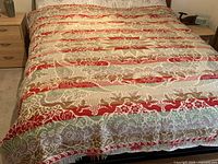 Full view of jacquard woven coverlet draped over a bed showing central starburst pattern and stripes in red, green, and beige.