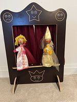 Puppet theatre frame with burgundy curtain, with two puppets attached and displayed upright.