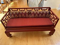 Full front view of the lacquered Oriental couch with red wood and red seat cushion, with decorative patterned silk back cushions.