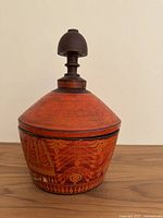 Front view of large antique lacquered wood container with detailed floral and geometric design and a dark wood finial on top.