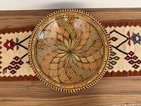Top-down view of the Moroccan ceramic bowl on a wood surface with the woven mat underneath showing colors and patterns of both items.