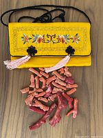 Yellow fabric pouch with floral embroidery containing red and pink coral chunks spread around it.