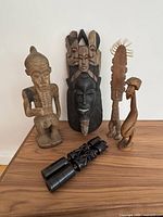All six African carvings and masks arranged together on wood surface showing diversity in size and shape