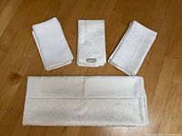 Folded white damask tablecloth with three stacks of folded napkins placed on wooden floor.