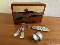 Three pieces of silver Indigenous jewellery (ring, earrings, salmon brooch) displayed with wooden marquetry box