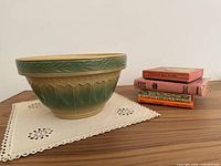 Mixing bowl on lace edged linen with stack of five vintage cookbooks to the side on a wood surface.