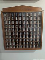 Front view of wooden display case holding 100 assorted thimbles visible through plexiglass cover.