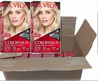 Open cardboard box containing 12 new boxes of Revlon Colorsilk Beautiful Color permanent hair dye in Ultra Light Blonde #04 shade, showing front packaging with model and branding.