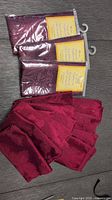Three packs of new linen napkins in original packaging, red/burgundy color with floral embossing, and several loose used napkins of the same design.