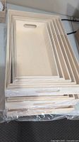 Stacked sets of unfinished wooden trays with handles, shrink-wrapped in plastic.