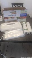 Photo showing Seal a Meal vacuum food sealer machine with box and three rolls of vacuum sealing bags on a table.