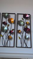 Two metal flower wall hangings with colorful dimensional flower petals framed in black rectangular frames.