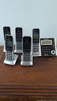 Group photo of 5 Panasonic cordless phones including 4 handsets and 1 base station with keypad and display screen.