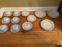 Full set of six cups, six saucers, six dessert and salad plates laid out on hardwood floor.