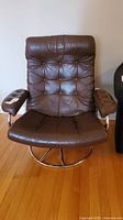 Front view of brown leather tufted swivel chair showing seat, back, armrests and chrome base