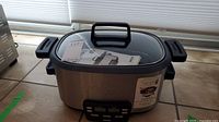 Front view of Cuisinart MSC 600 slow cooker with glass lid and original manual inside.