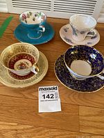 Four cups and saucers displayed on wood surface showing varied designs and colors.