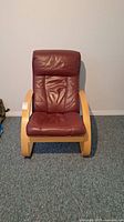 Front view of the easy chair showing brown leather seat and back with wood arms and legs.