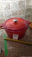 Red enameled cast iron pot with lid on kitchen countertop, measuring tape shows 10 inches diameter.