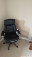Full view of black La-Z-Boy office chair with floor protector mat behind it in corner of room.