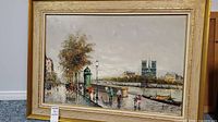 Full view of the framed painting showing river, buildings, a horse and carriage, and pedestrians.