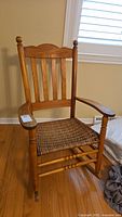 Front view of vintage wooden rocking chair showing wicker seat, spindle backrest, turned armrests, and wooden rockers.