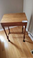 Side view of vintage wooden side table showing spindle legs and metal castors on hardwood floor.