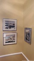 Three framed signed nautical prints hanging on a beige wall corner.