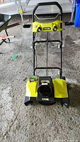 Front view of yellow and black Ryobi snow blower showing the intake and handlebar.