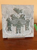 Front view of soapstone carving showing six Inuit figures and one figure above, all carved in dark green soapstone with etched white details on a gray background.