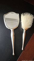 Hand mirror and hairbrush with sterling silver handles on a dark surface