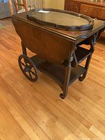 Full side view of the wooden tea cart showing its structure, fold-down side, two shelves, and large round decorative wheels.