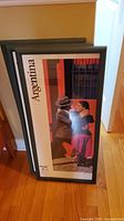 Framed Argentina travel print with tango dancers in black frame leaning against wall.