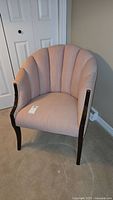 Front view showing the pink fabric upholstery, scalloped backrest, and carved dark wood armrests and legs of the tub chair.