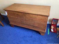 Front view of vintage wooden blanket box showing rectangular shape, hinged lid with keyhole, and natural wood finish.
