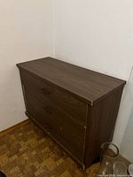 Full angle view of the veneer 3 drawer dresser placed against a wall on a hardwood floor.