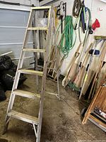 General side view of the 6-foot aluminum ladder positioned in garage surroundings showing six-step folding construction and rear support braces.