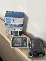 Atoma blood pressure monitor displayed with cuff and original box, showing the device screen and buttons.