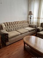 Full view of the beige three-seater sofa bed showing tufted backrest, wooden armrests, and cushions.