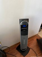 Full view of black and silver Bionaire tower heater plugged in, digital display showing controls and power on.