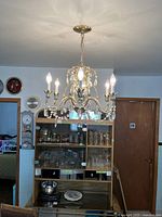 View of gold accented chandelier hanging in a kitchen setting with six lit candle bulbs and crystal decorations.