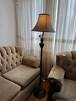 Full view of the brown metal floor lamp next to tufted beige furniture in front of sheer curtains.