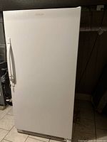 Front view of white Frigidaire upright freezer on tiled basement floor