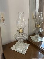 Photo of a single glass antique lantern on a reflective square base, showing the full length from base to chimney.