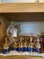 Shelf with small blue glasses with gold tops and handles, displayed in a row with a silver teapot partially visible at the back.