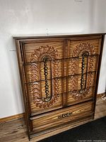 Full view of the ornate wooden high boy dresser showing carved sunburst design and metal handles.