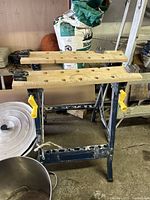 Front view of Job Mate workbench showing metal frame, wooden work surfaces with holes, and yellow clamps.