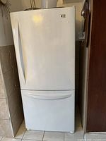 Front profile of white LG refrigerator with top fridge door and bottom freezer drawer.