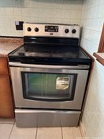 Front view showing stainless steel body, black ceramic glass cooktop with four zones, digital control panel and oven door with window
