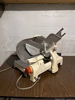 Photo of the entire meat slicer showing white body, metal blade, and carriage assembly on a wooden table.